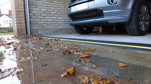 An installed garage door threshold stopping water and leaves from entering a garage with a car in it