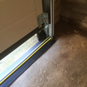 A notched garage door threshold seal affixed to the side of the garage door