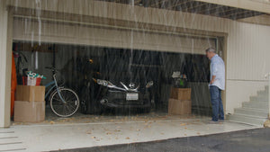 A man standing in front of a garage in the rain with leaves and water making their way inside